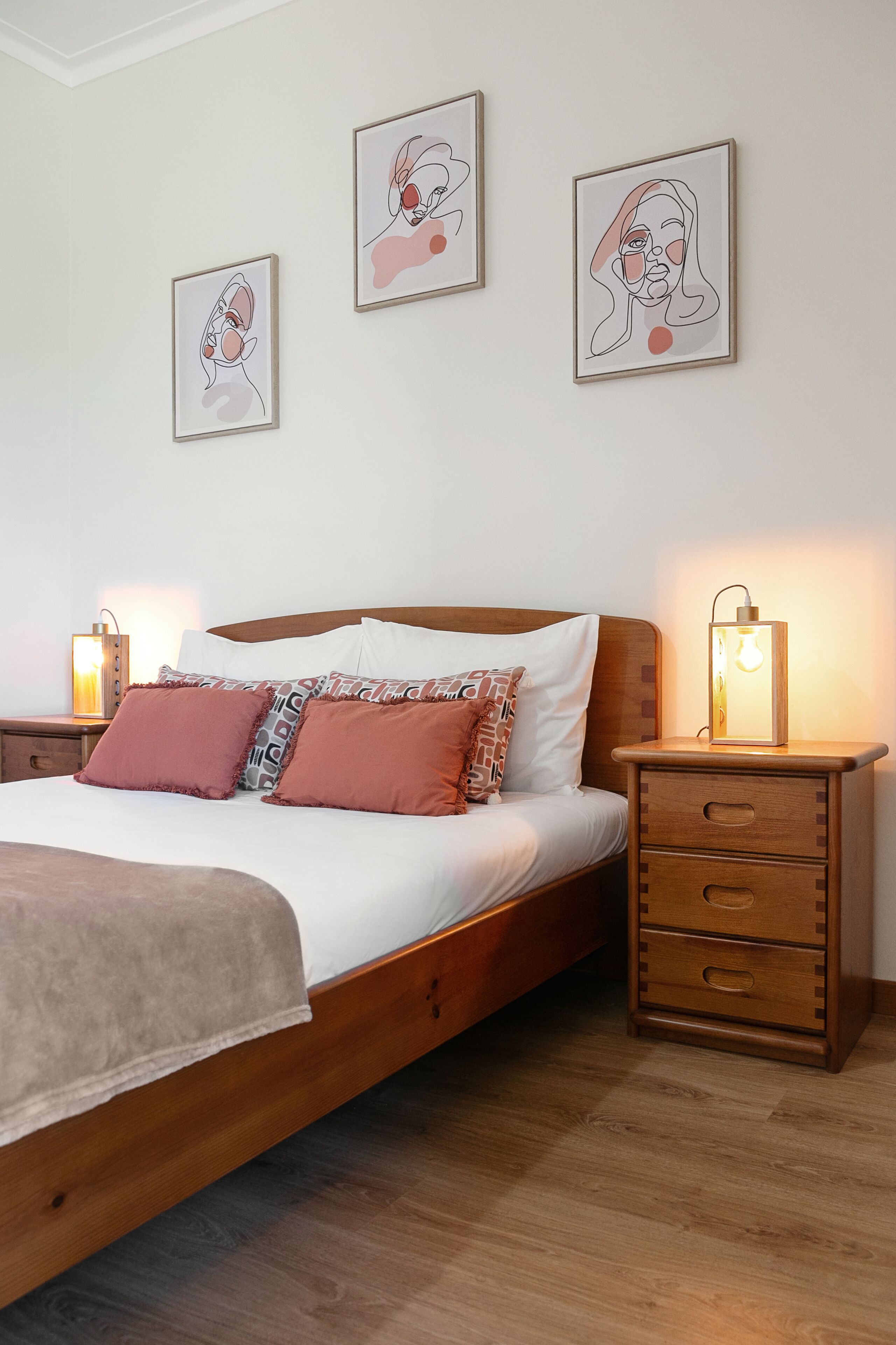 A neatly made bed with a wooden headboard, two bedside tables with lamps, and three framed artworks on the wall.