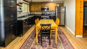 Une cuisine moderne avec des meubles de rangement noirs, une table à manger en bois et un tapis à motifs.