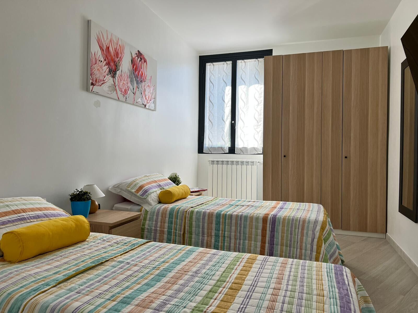 A bedroom with two beds, a window with curtains, a radiator, and a wooden wardrobe.