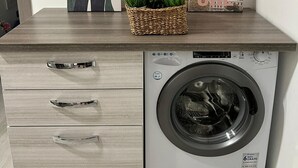A laundry area with a washing machine, a wooden cabinet with drawers, and three framed artworks on the wall.