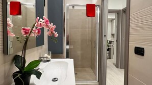 A modern bathroom with a white sink, a mirror, a potted orchid, and a shower area.