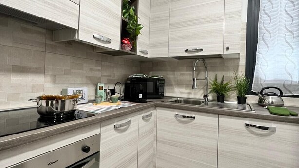A modern kitchen with light wood cabinetry, stainless steel appliances, and a built-in oven.