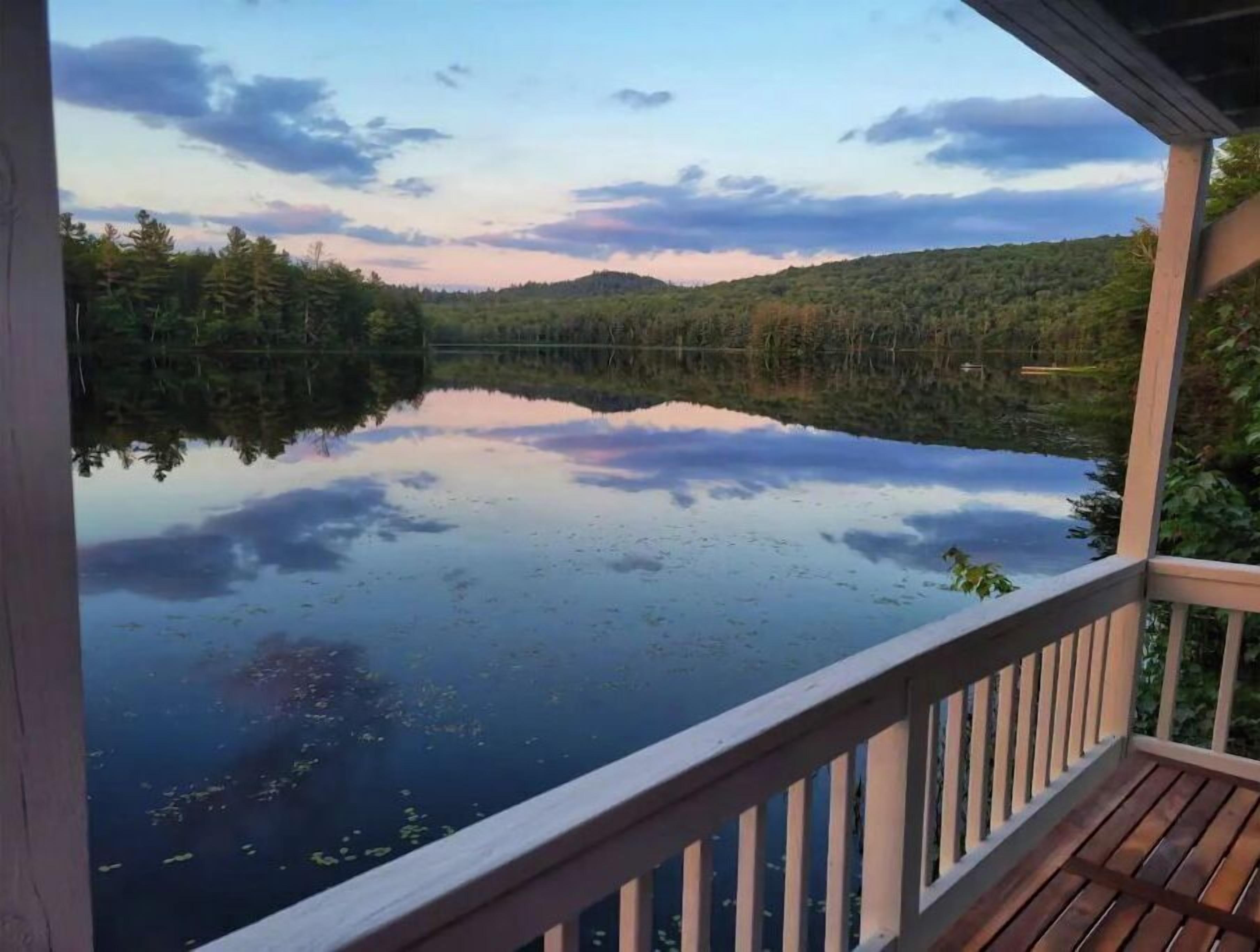 Une terrasse en bois surplombant un lac paisible, dont les eaux reflètent les arbres et un ciel dégagé.