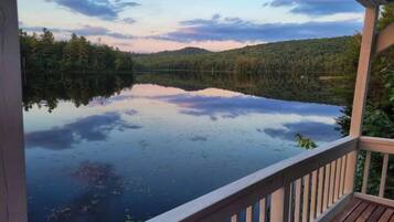 Une terrasse en bois surplombant un lac paisible, dont les eaux reflètent les arbres et un ciel dégagé.