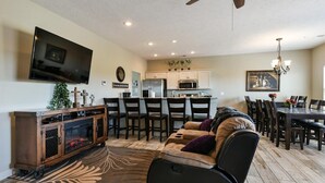 A modern living room with a sofa, a TV, a fireplace, and a dining area with chairs and a table. - The LUX Stonebridge - No Stairs! Close to SDC! (Reeds Spring)