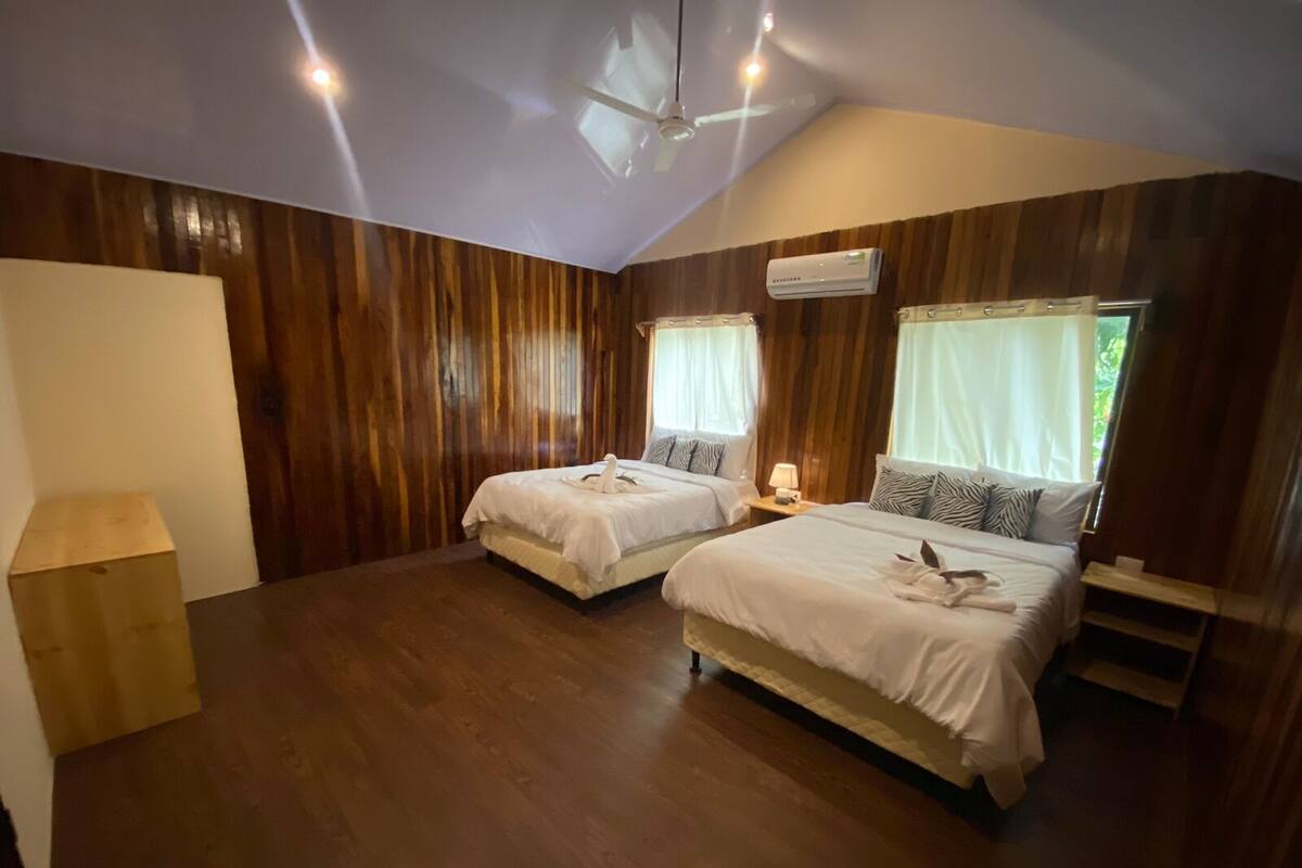 A room with two beds, wooden paneling, a ceiling fan, and an air conditioning unit.