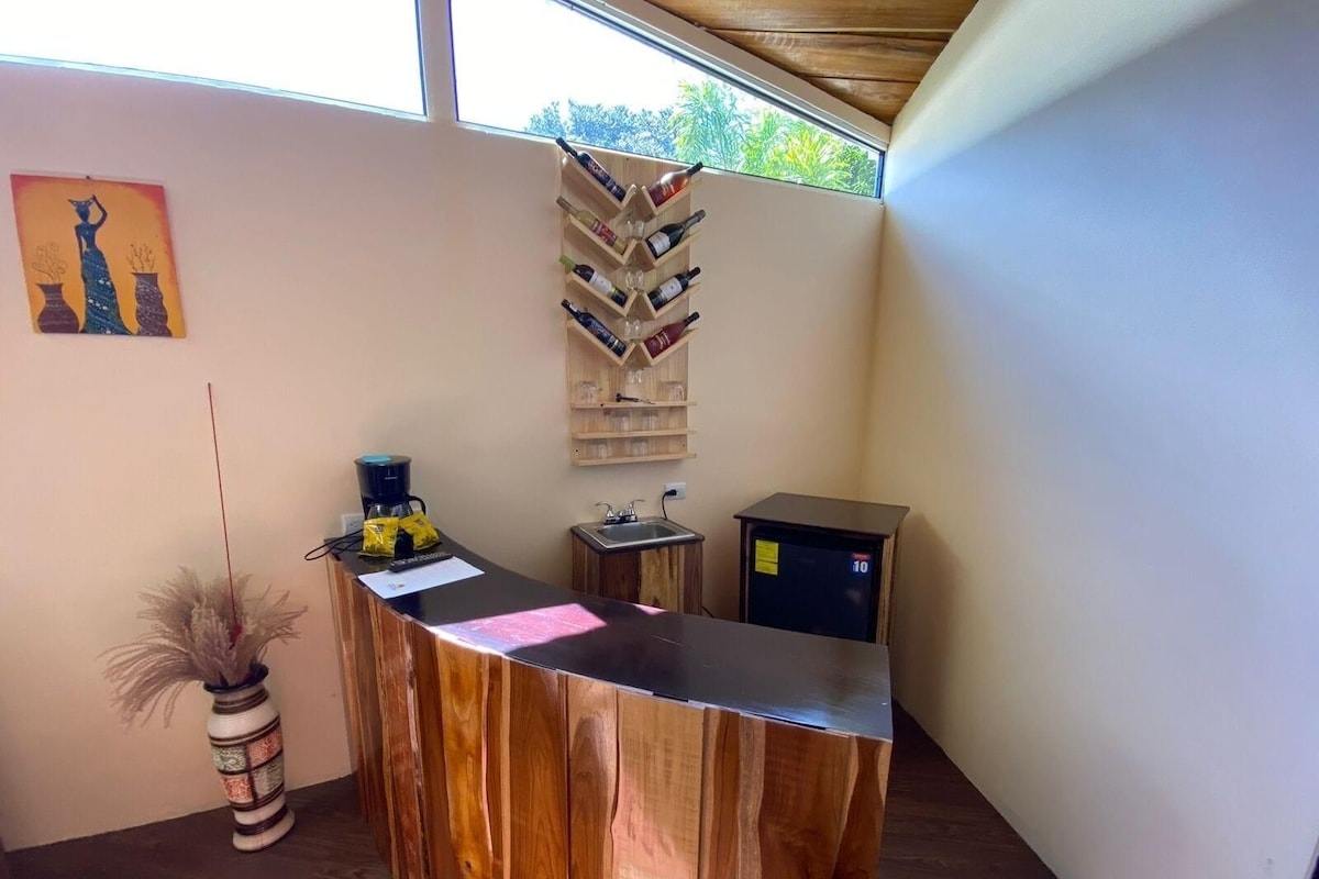 A reception desk with a wooden finish, a coffee machine, a vase with dried plants, and a wall-mounted wine rack.