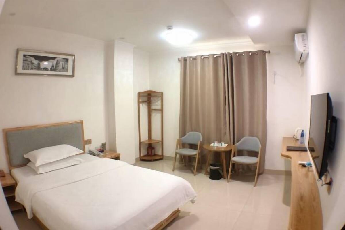 A hotel room with a bed, a desk with a chair, a television, and a picture on the wall.