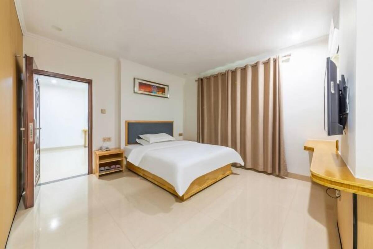 A hotel room with a bed, bedside table, a TV, and a door leading to another room.
