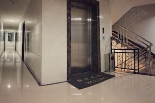 Un vestíbulo de hotel con piso de mármol, un ascensor y una escalera con barandilla de metal.