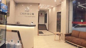 A reception desk with a sign, a sofa, and a view of the street through a window. - Huiyue Fashion Apartment (Haifeng)