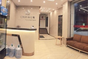 A reception area with a reception desk, a sofa, and a staircase leading to an upper floor. - Huiyue Fashion Apartment (Haifeng)