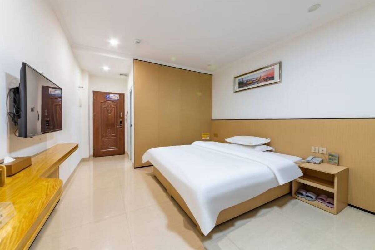 A hotel room with a bed, a TV, a desk, a wardrobe, and a picture on the wall.