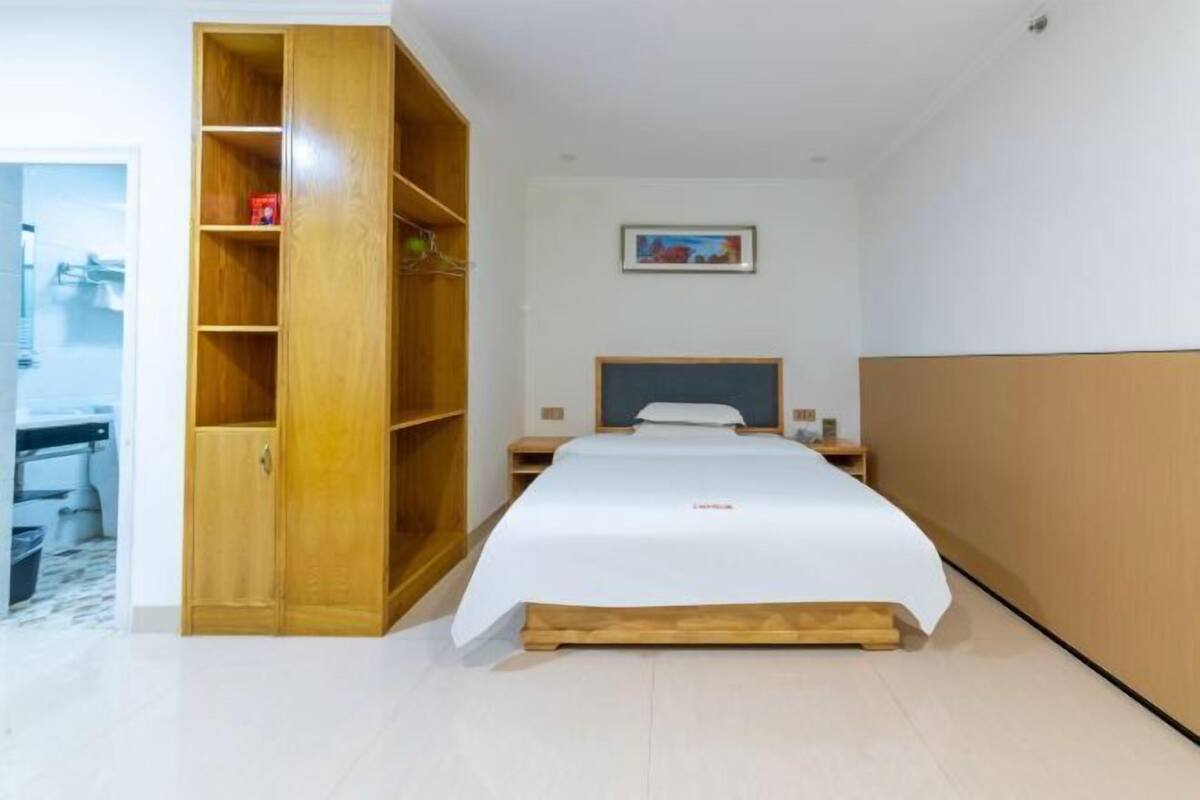 A bedroom with a bed, a wooden wardrobe, a nightstand, and a framed picture on the wall.