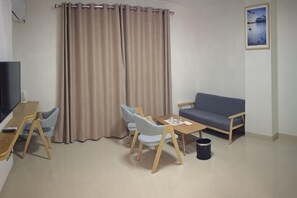 Una habitación con sofá, una mesa con sillas, televisor y cortina.
