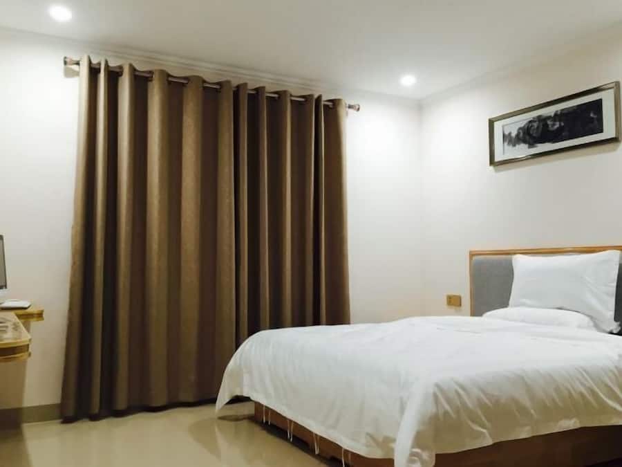 A hotel room with a bed, a desk with a computer, and a window with curtains.