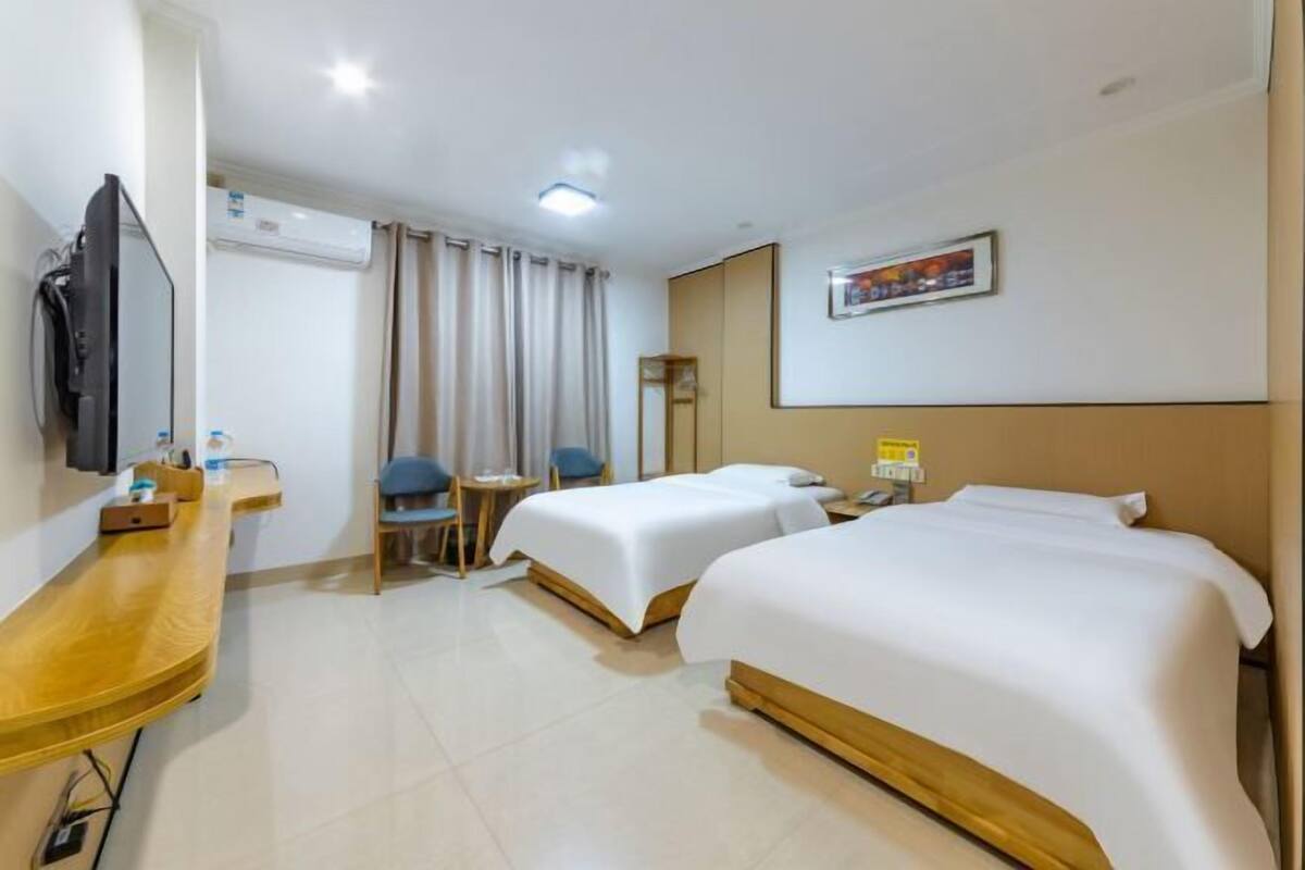 A hotel room with two beds, a desk, a chair, a TV, and a window with curtains.