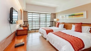 Habitación de hotel con dos camas, televisión, escritorio y ventana grande.