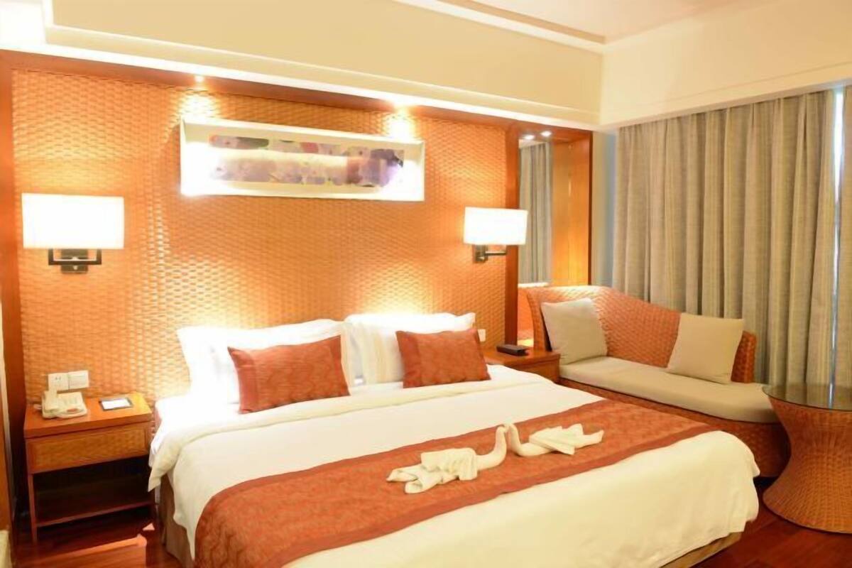 A hotel room with a large bed, a sofa, two bedside lamps, a nightstand, and a window with curtains.