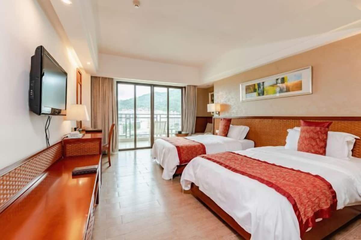 A hotel room with two beds, a television, a desk, and a large window.