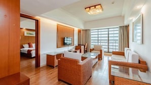 Una habitación de hotel con piso de madera, un área de comedor con mesa de vidrio, un sofá y un televisor montado en la pared.
