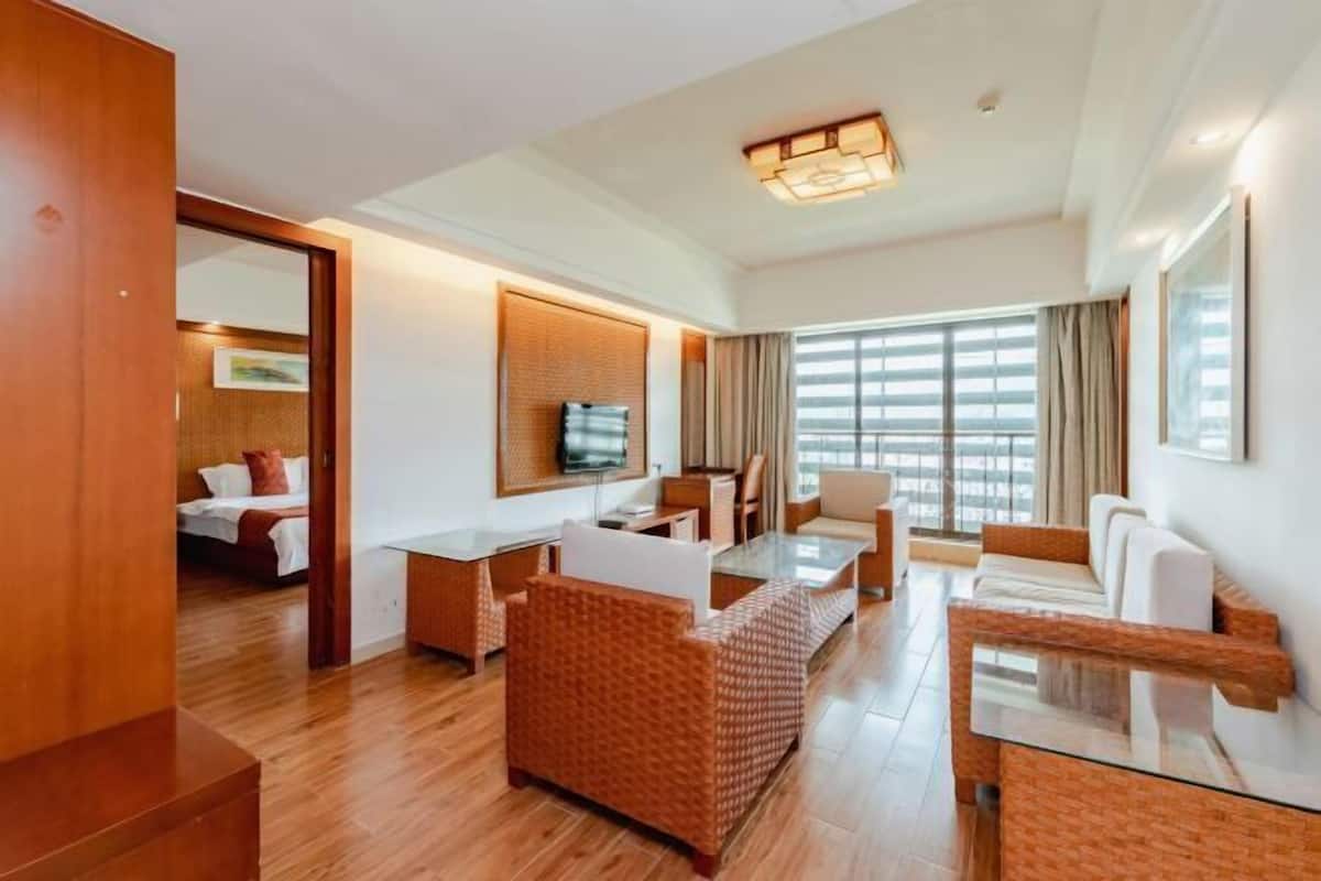 A hotel room with a wooden floor, a dining area with a glass table, a sofa, and a TV mounted on the wall.