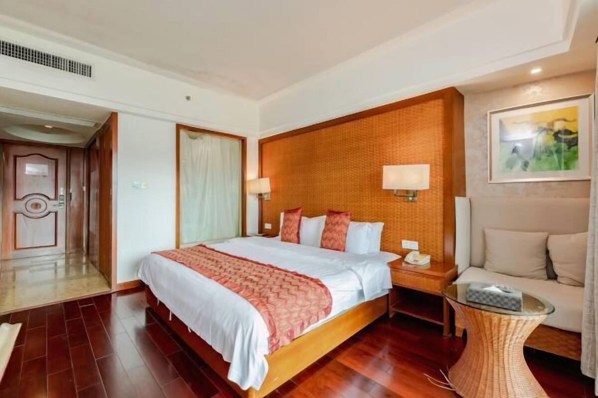 A hotel room with a large bed, a bedside table with a lamp, a small round table, and a sofa.
