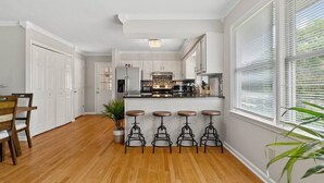 A kitchen with white cabinets, a central island with stools, and a dining area with a wooden table and chairs.