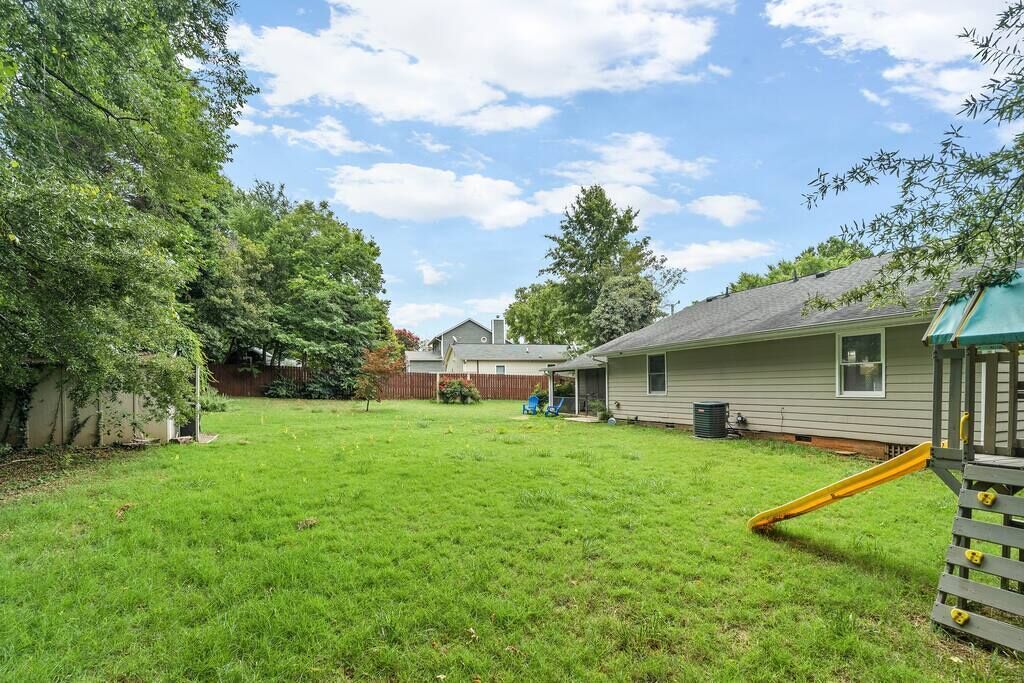 Un jardin avec une pelouse verdoyante, une aire de jeux et une maison en arrière-plan.