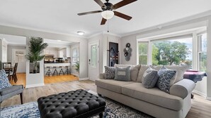 A spacious living room with a grey sofa, black ottoman, and a ceiling fan.
