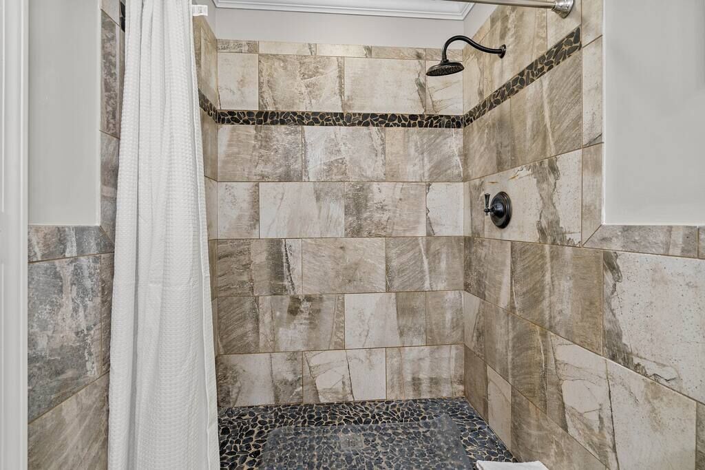 Ducha con cabezal de ducha tipo lluvia, paredes con azulejos y cortina de baño.