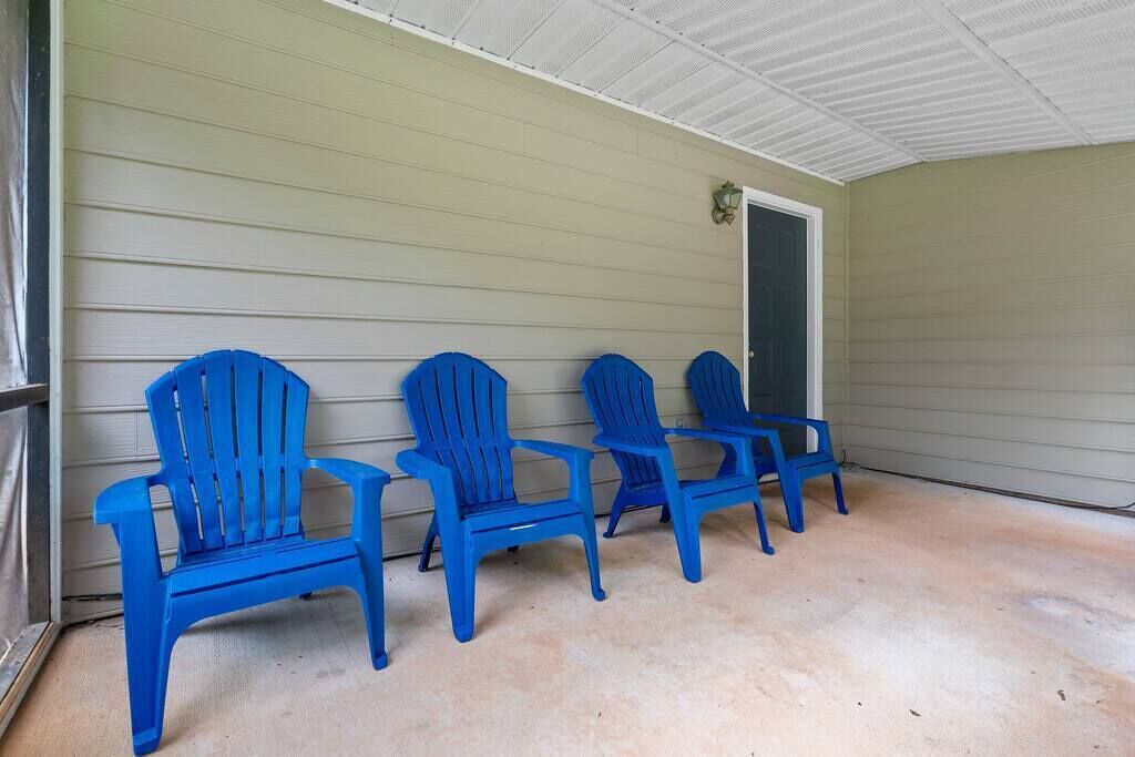 A covered porch with four blue Adirondack chairs aligned against a beige wall.