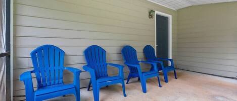 Eine überdachte Veranda mit vier blauen Adirondack-Stühlen, die an eine beige Wand gelehnt sind.