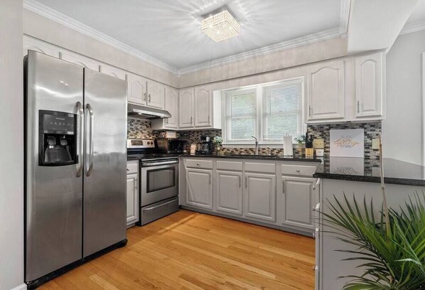 A modern kitchen with stainless steel appliances, white cabinetry, and a wooden floor.