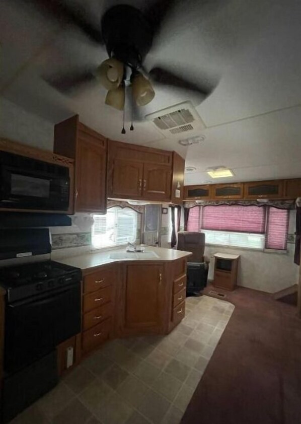 A compact kitchen with wooden cabinets, a black stove, and a ceiling fan.