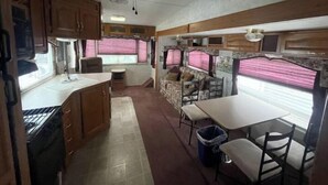 A compact RV interior with a kitchenette, a dining area, and a seating area with curtains. - Charming 1-br RV, free parking by Pensacola Beach (Pensacola)