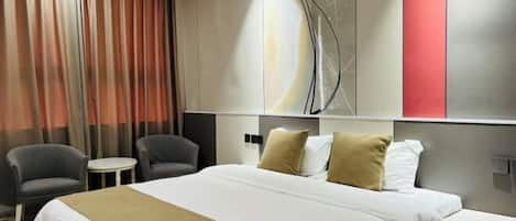 A hotel room with a large bed, two armchairs, a small table, and a wall with abstract art.