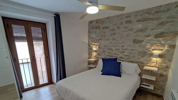Une chambre à coucher avec un lit, un ventilateur de plafond, un mur en pierre et un balcon avec une porte.