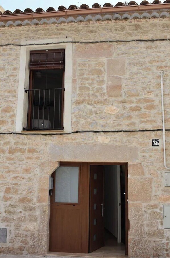 A stone building with a wooden door and a window with a metal grill.
