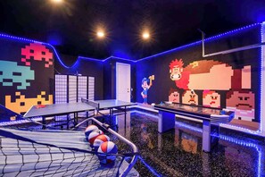 Une pièce équipée d’une table de ping-pong, d’un panier de basket et décorée de motifs artistiques pixélisés sur les murs.