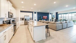 A modern kitchen with white cabinets, a central island, and a dining area with a sofa. - Huge 9BR Vacation Villa in Orlando | Near Disney (Kissimmee)