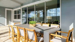 An outdoor dining area with a table and chairs, a basket of greenery, and a view through large windows. - Huge 9BR Vacation Villa in Orlando | Near Disney (Kissimmee)