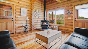 A log cabin interior with a central fireplace, wooden walls, and a cozy seating area. - Wildflower Retreat (Greer)