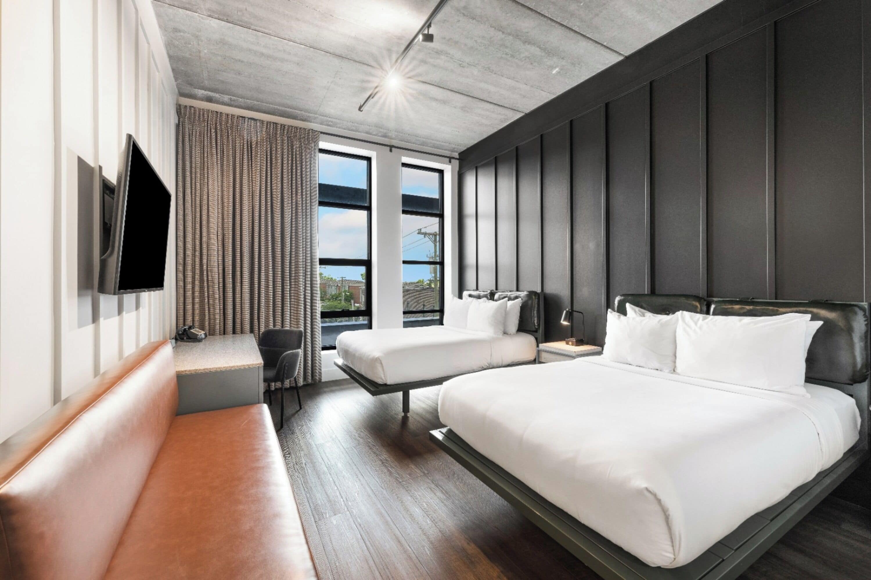 A modern hotel room with a large bed, a smaller bed, a seating area, a TV, and a window with curtains.