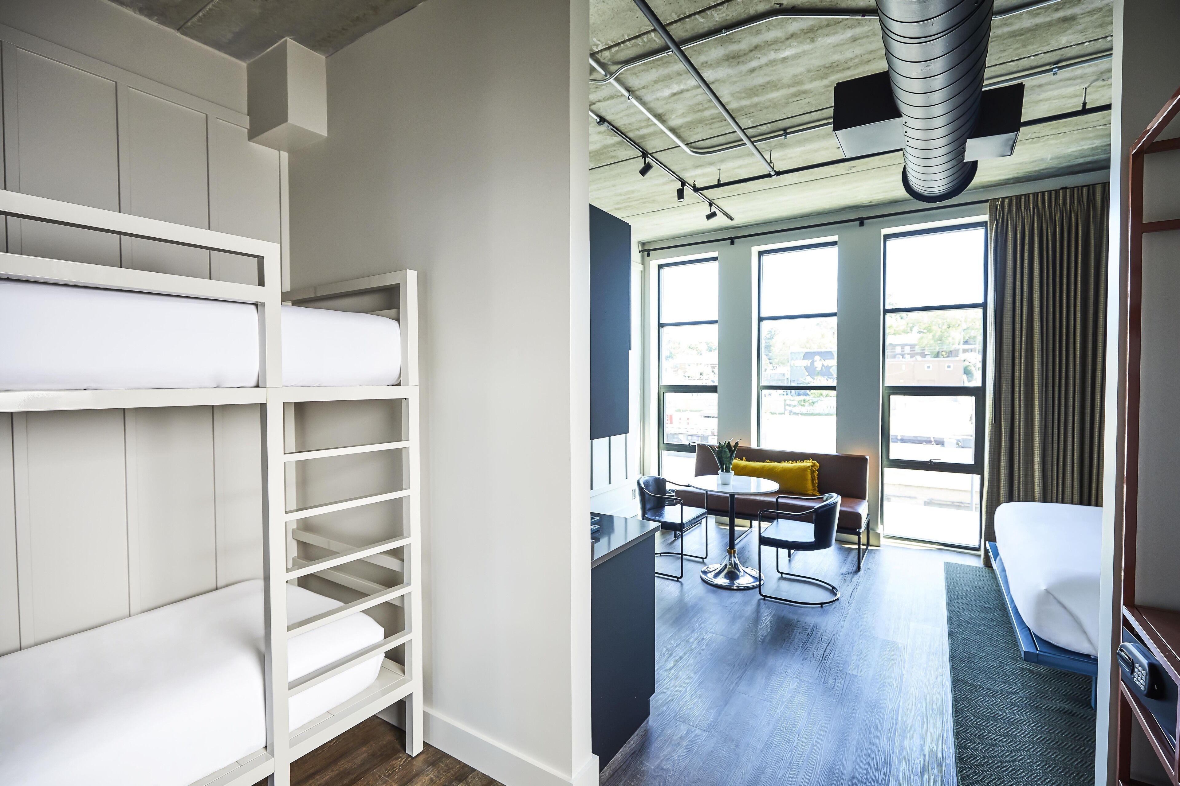 A modern hotel room with bunk beds, a dining area, and large windows.