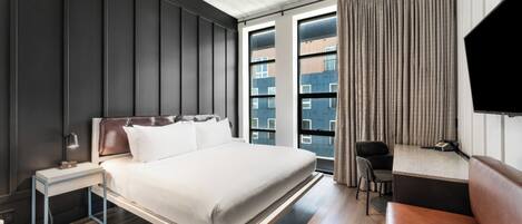Quarto de hotel moderno com uma cama grande, mesa de cabeceira e escrivaninha com cadeira.