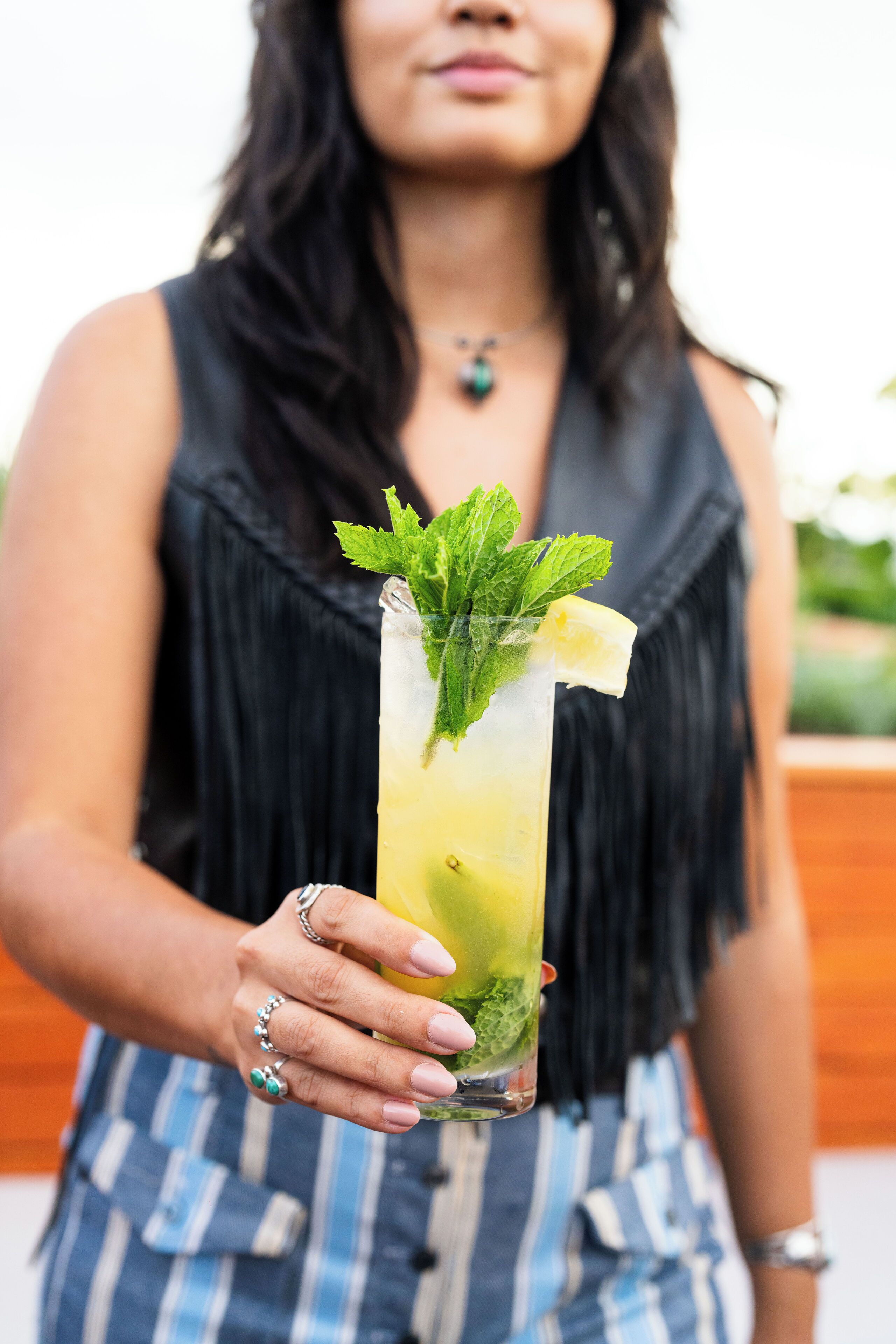 Une personne tenant un grand verre décoré d’une tranche de citron vert et de quelques feuilles de menthe.