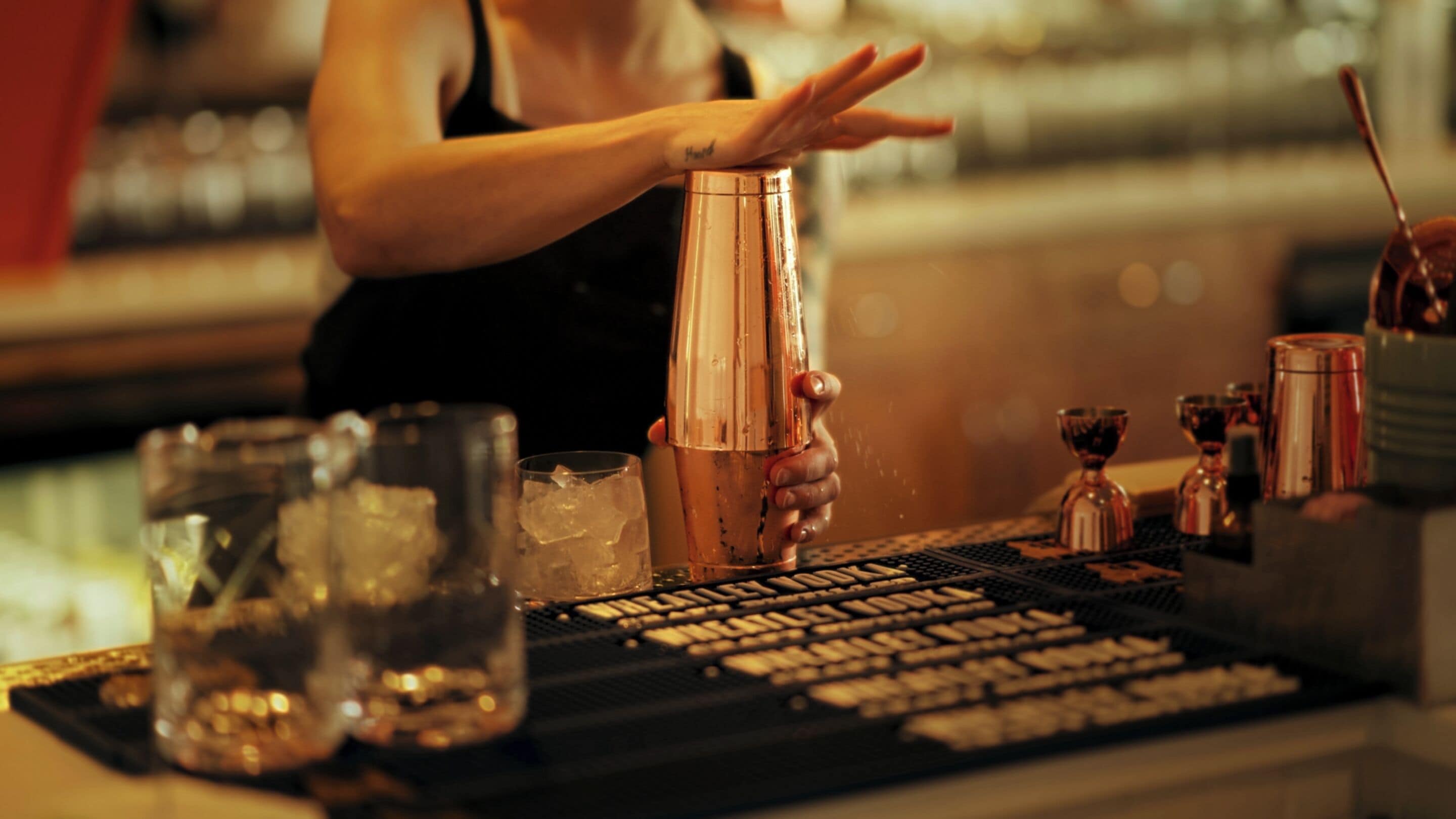 A bartender preparing a drink with a shaker, ice, and various bar tools on a counter.