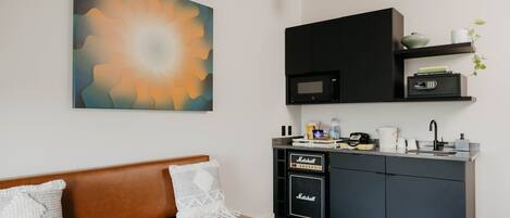 A modern kitchen with a microwave, coffee maker, and a small shelf with books and a plant.