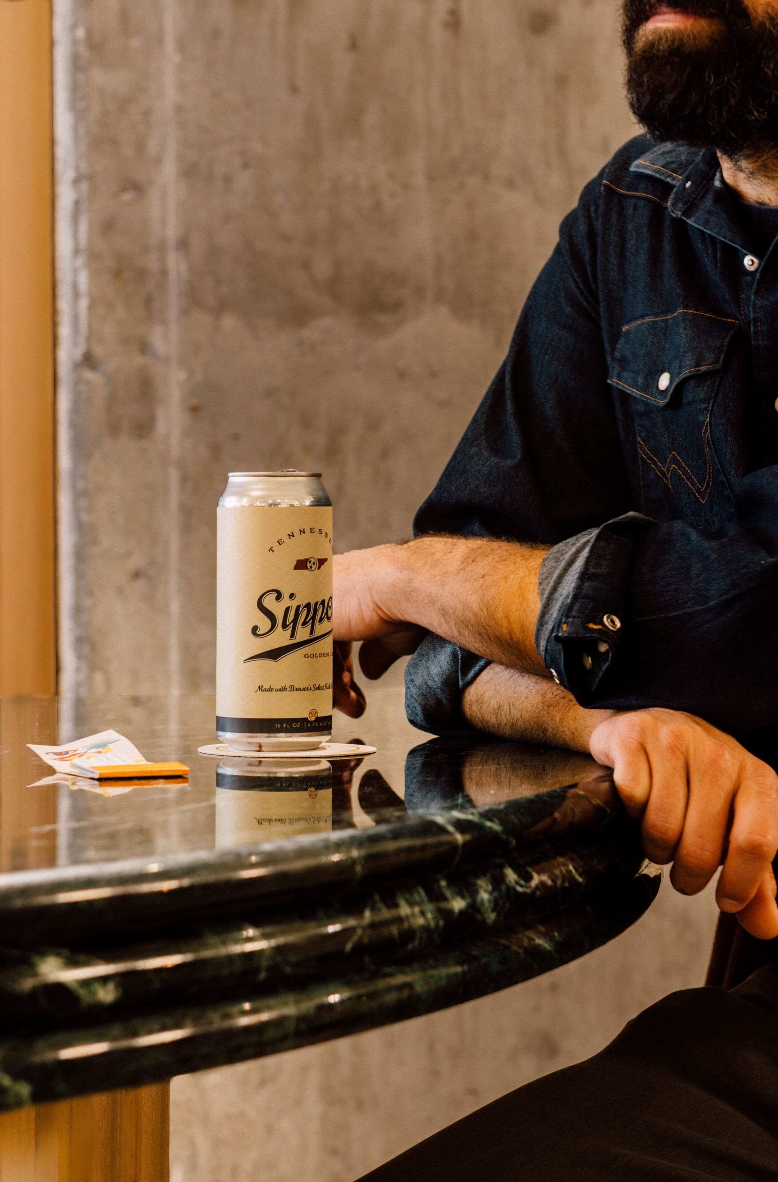 A person sitting at a table with a can of Sippin' Gold beer and a menu.